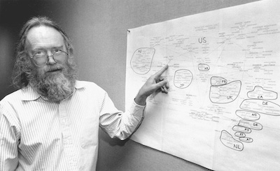 Jon Postel standing by a hand‐drawn diagram of the early internet.
